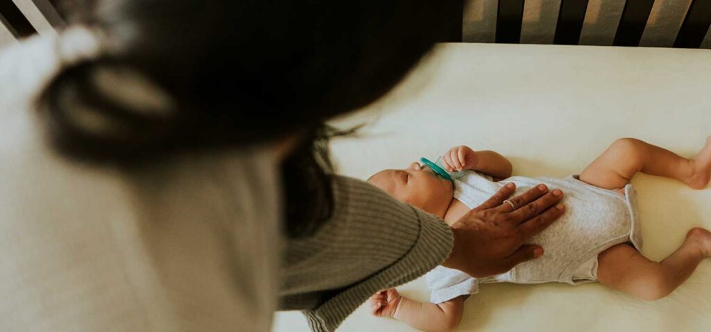 Newborn sleeping in a crib with their mother's hand comforting them