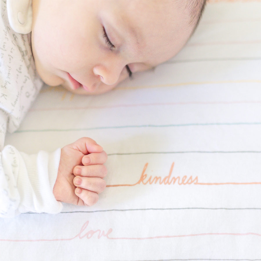 Baby sleeping with the word "kindness" written on the blanket